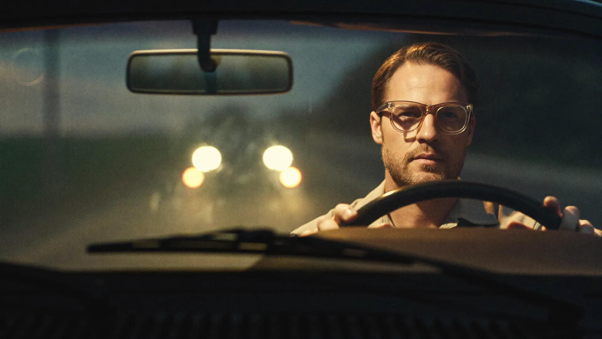 A wearer driving at night, oncoming headlights held as soft points through the lens — glare tamed.