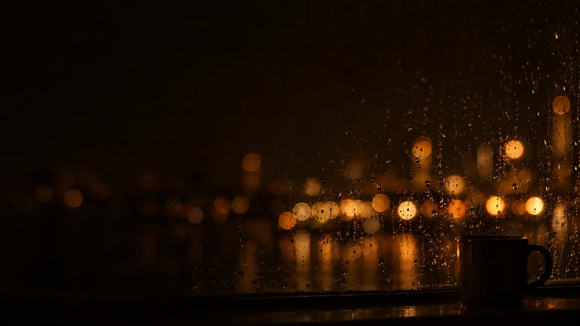 A night window: raindrops sharp on the glass, distant city lights melted into soft round blurs.