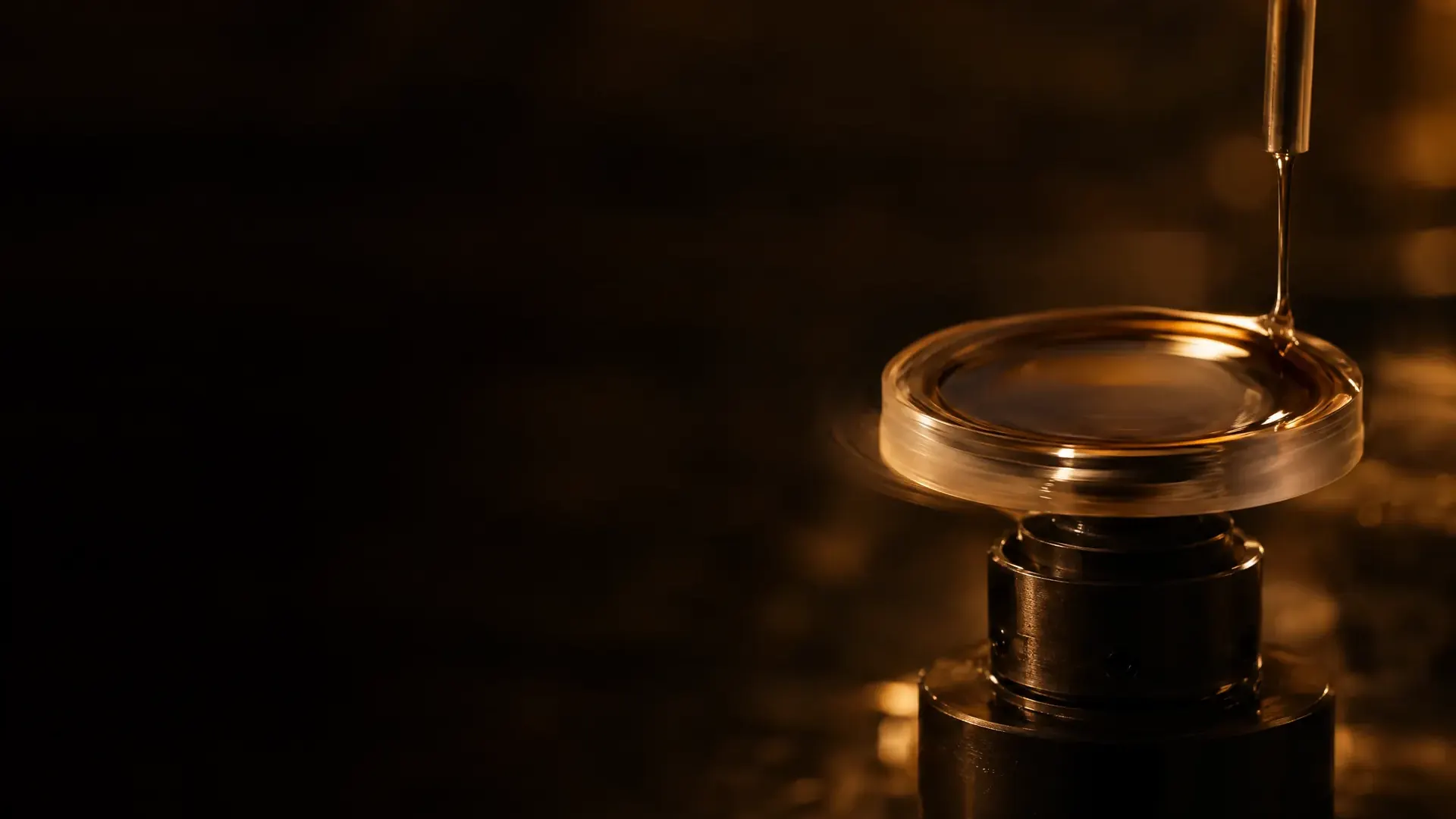 A lens spinning on a chuck as a thin liquid coating spreads across it.