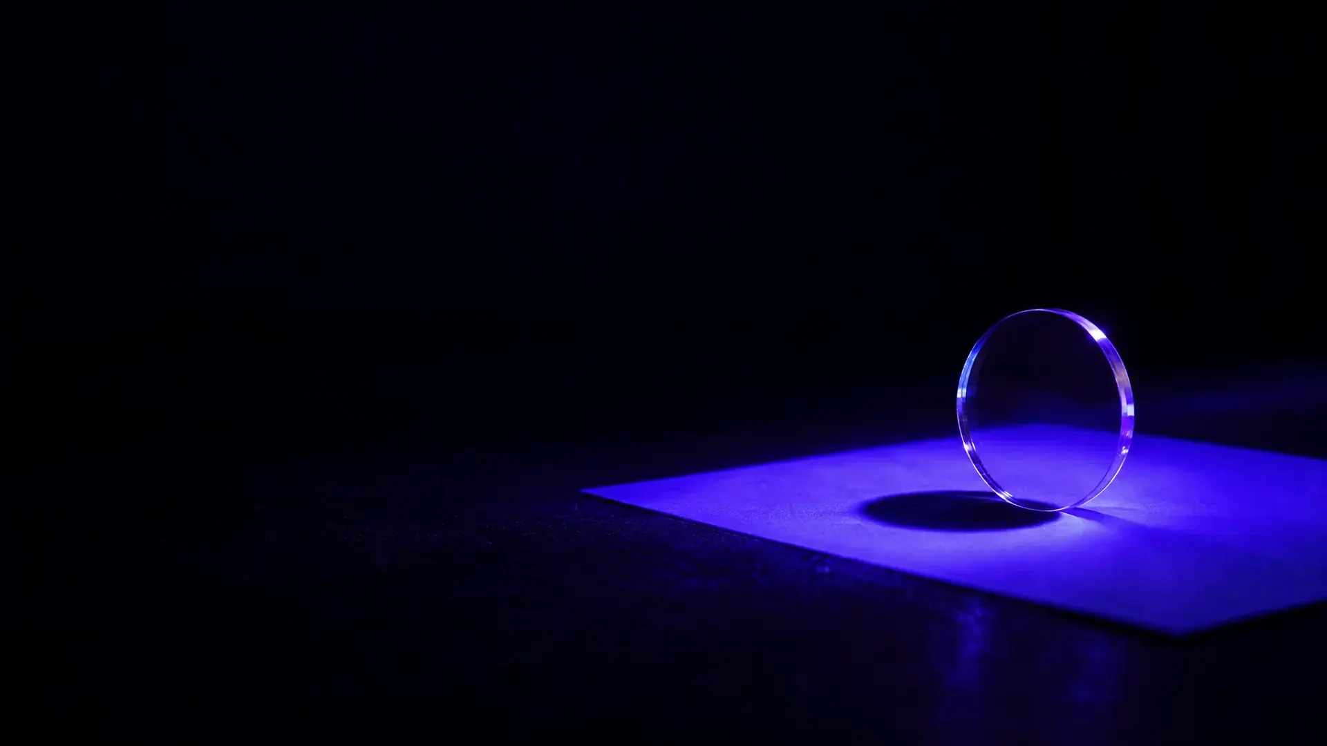 A clear lens in violet ultraviolet light, casting a dark shadow on a glowing fluorescent sheet.