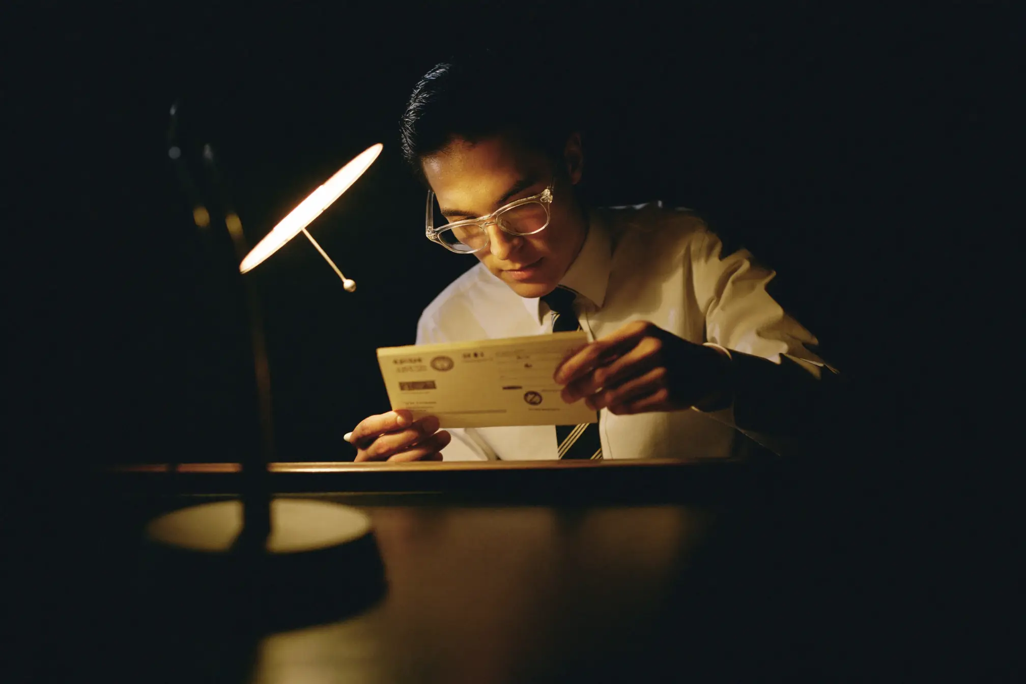 A bank teller examining a blank check under a warm desk lamp.