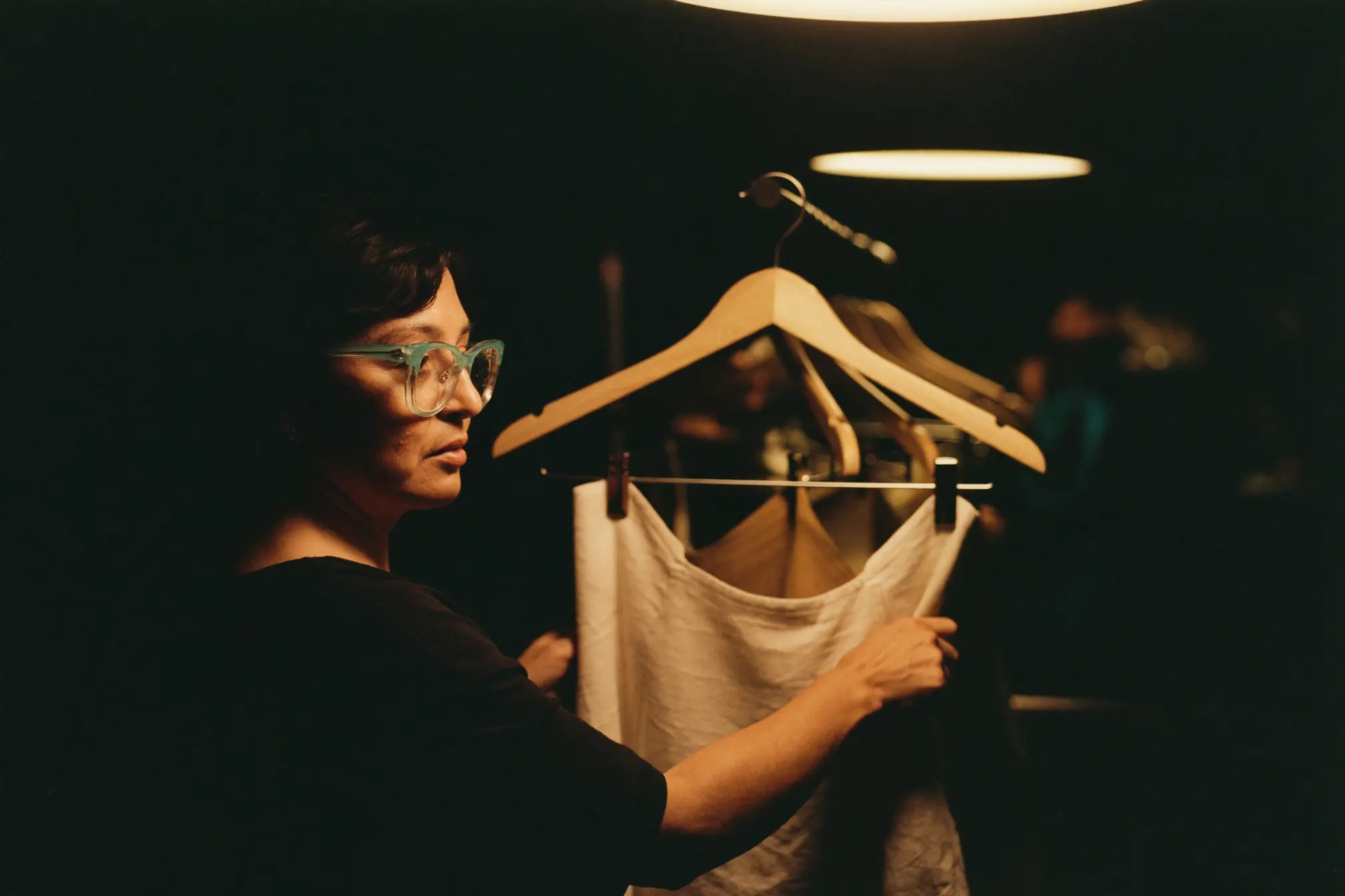 A boutique owner adjusting a cream linen garment on a wooden hanger.