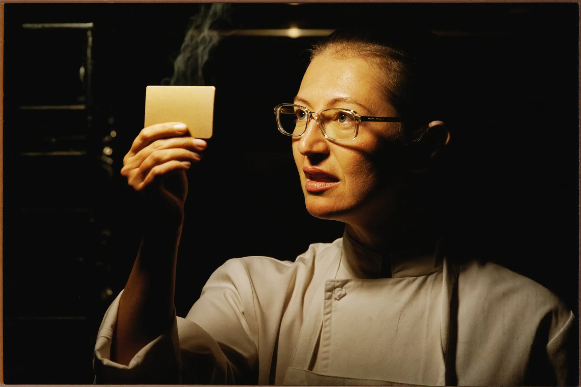 A chef glancing up from a small blank ticket whose face is turned away.