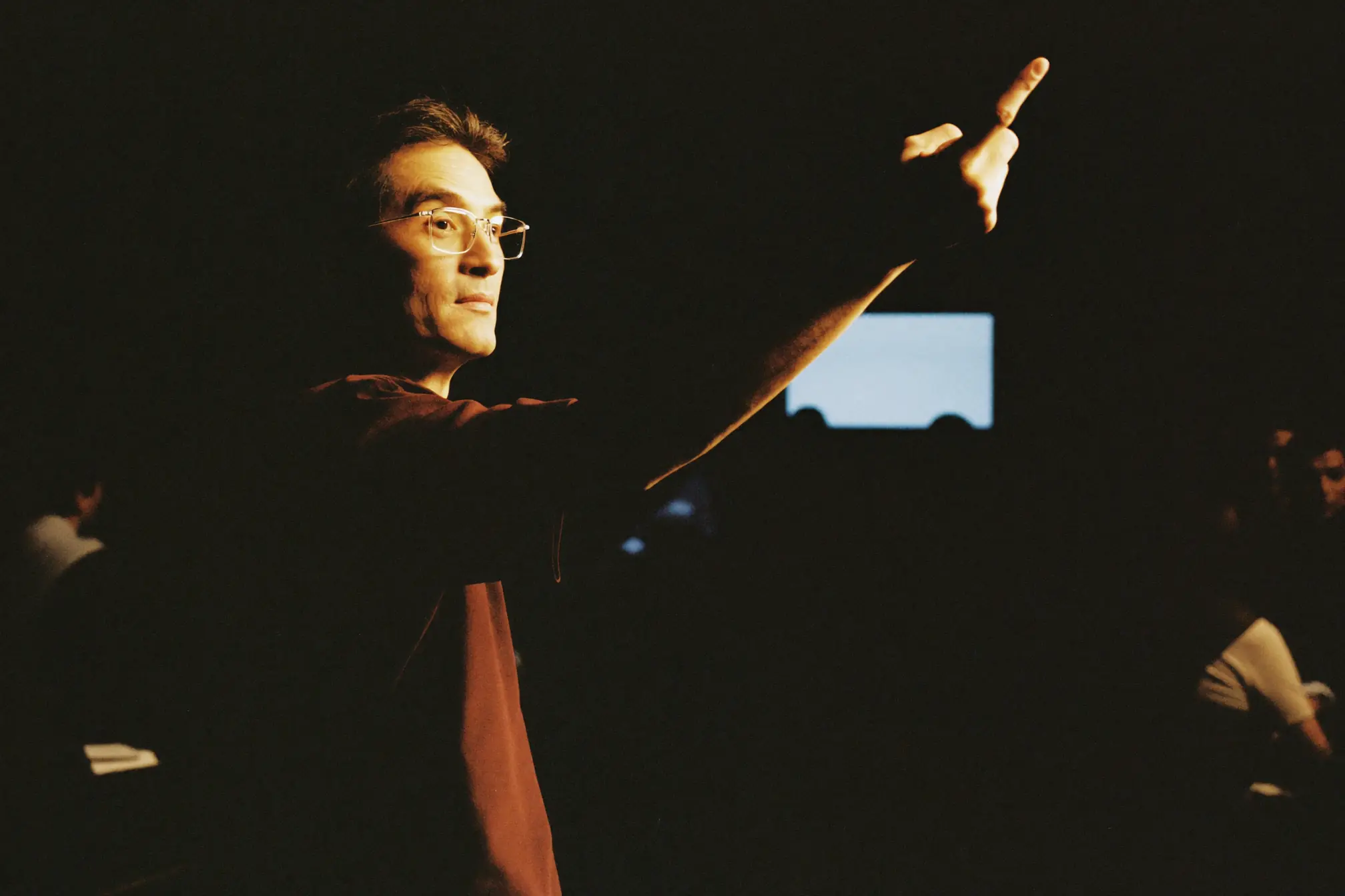 A corporate trainer gesturing to a small dark room of listeners.