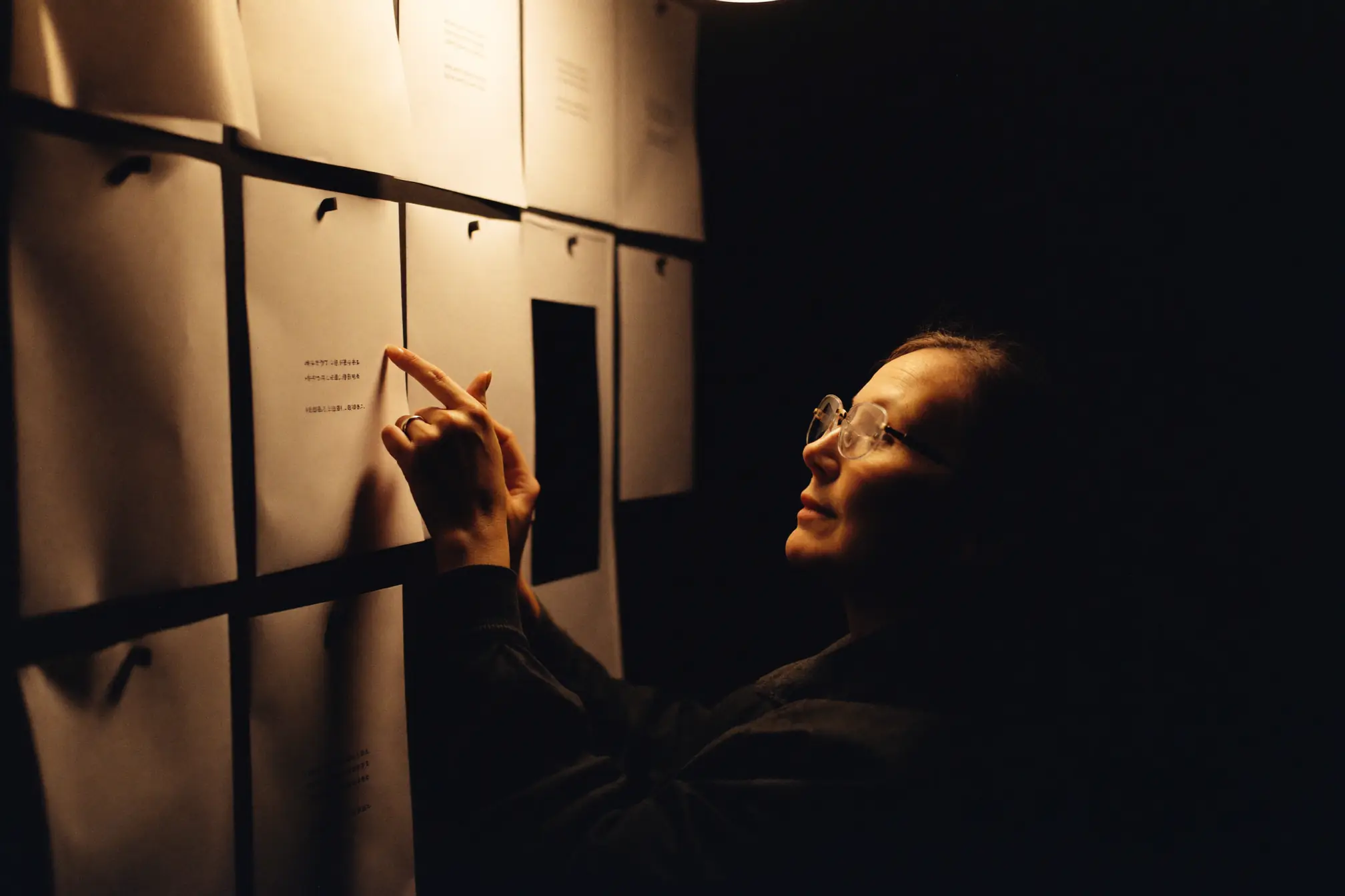 A creative director reviewing blank layout boards pinned to a dark wall.