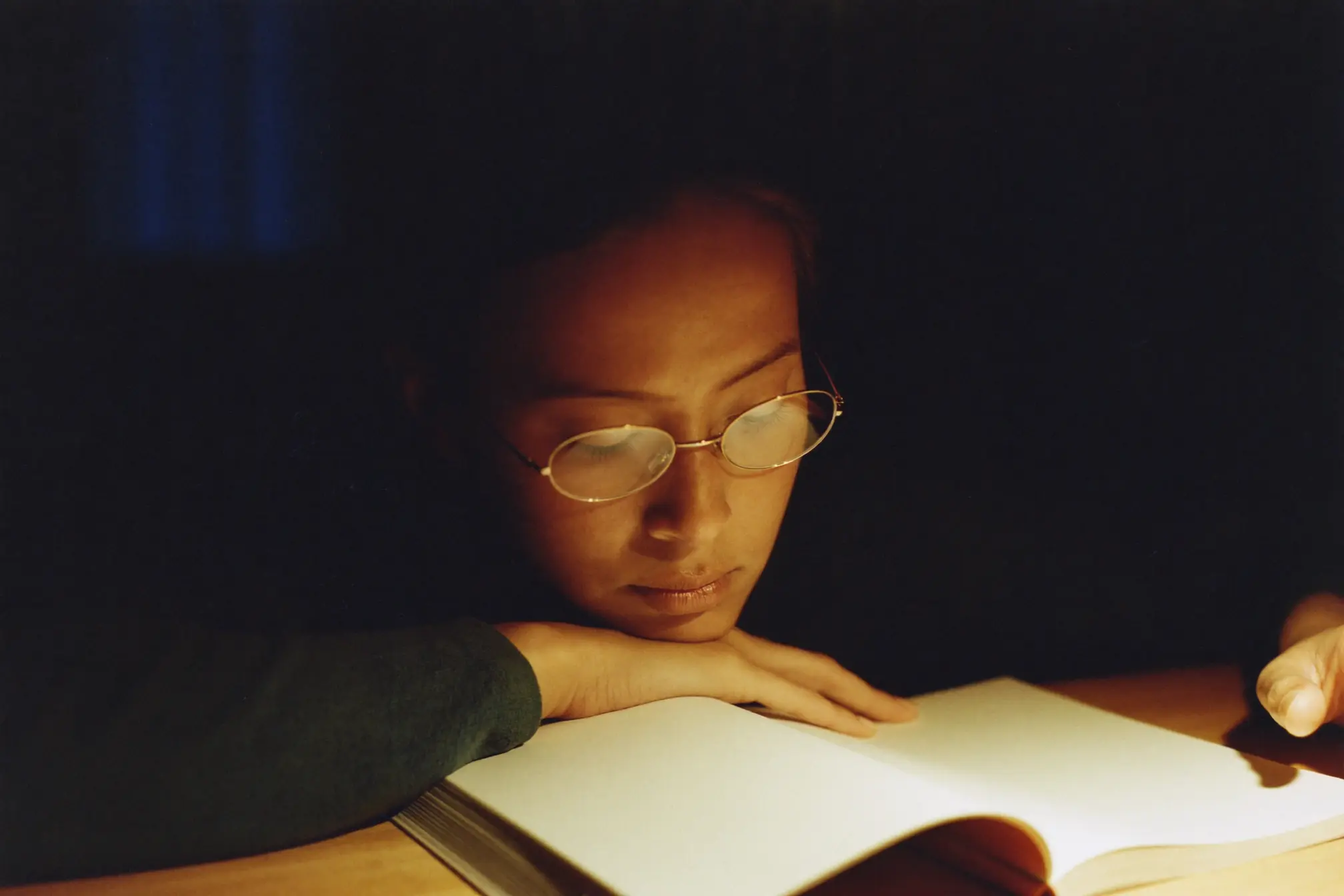 A home tutor leaning over a student's blank exercise book at a wooden table.