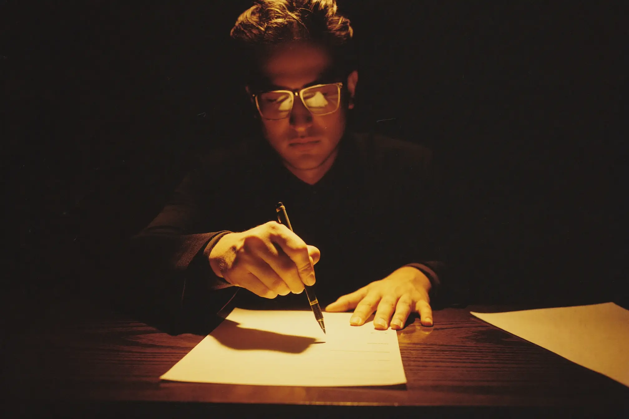 An insurance agent offering a pen over a blank form at a dark wooden table.
