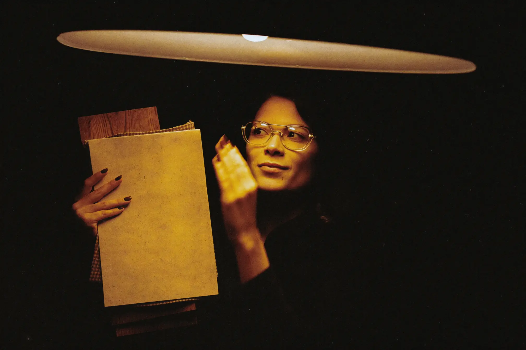 An interior designer holding fabric and wood samples close to a warm lamp.