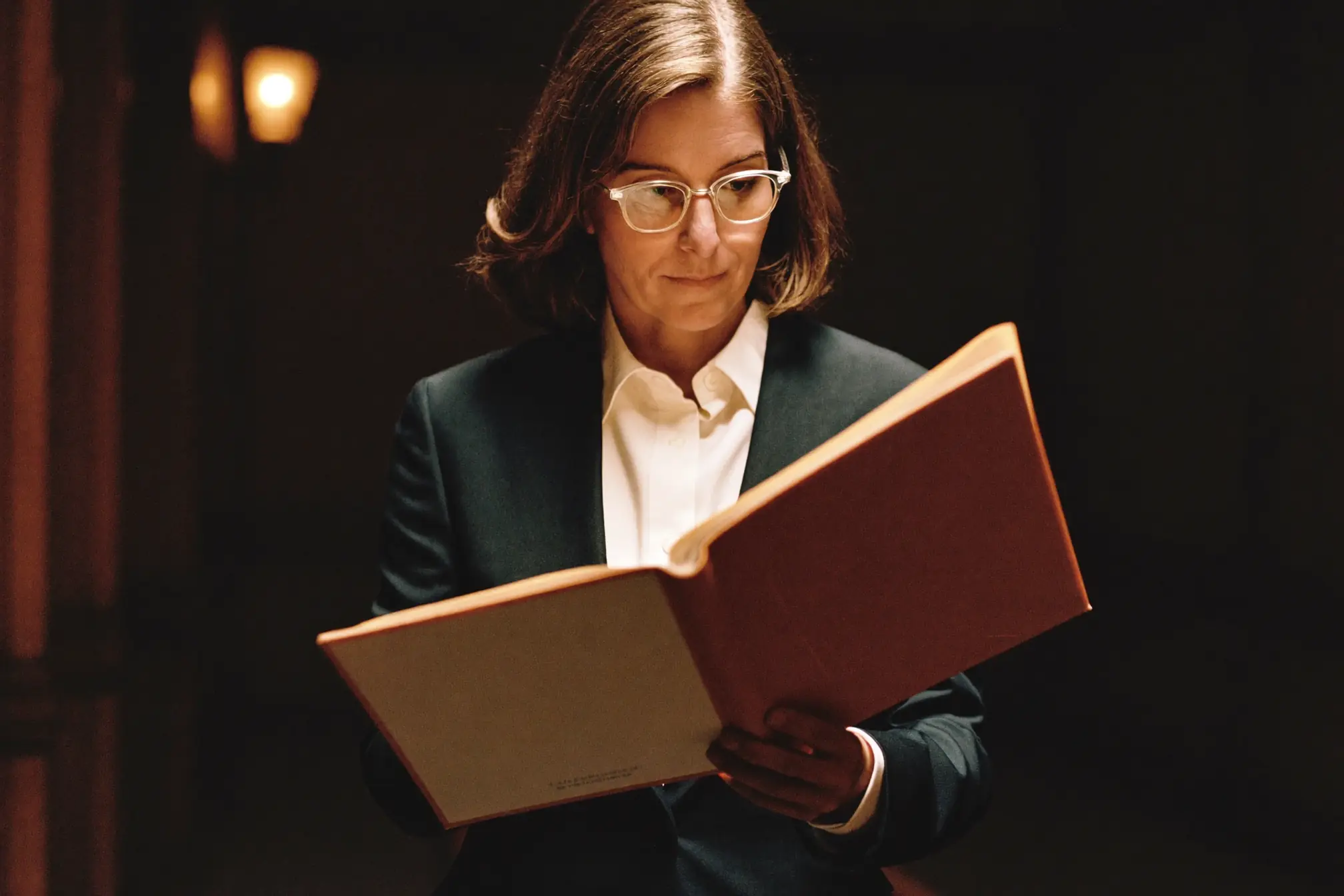 A trial attorney in a dark suit reading a bound case file in a courthouse corridor.