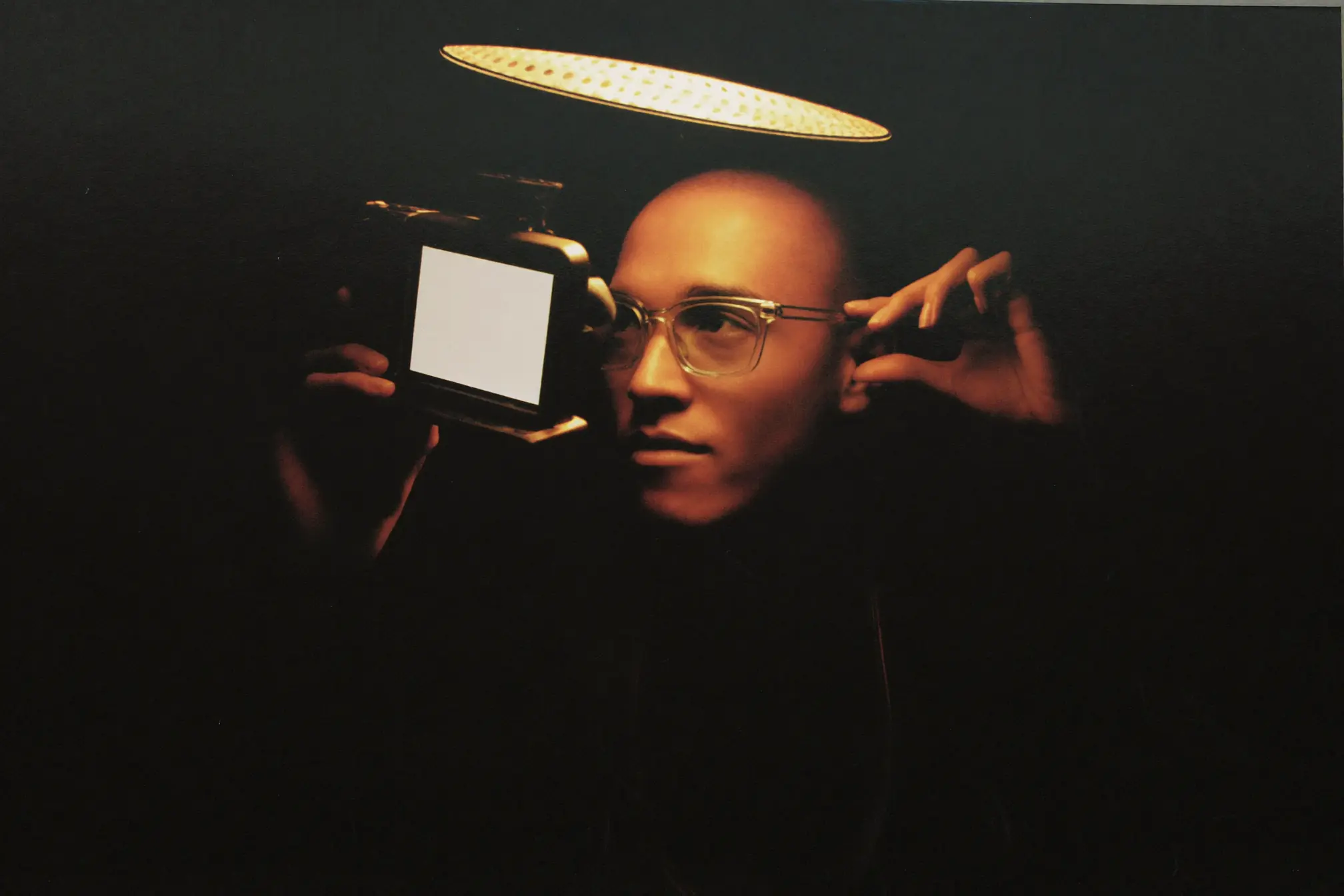 A photographer checking the back of a camera whose screen is a soft warm-white blank.