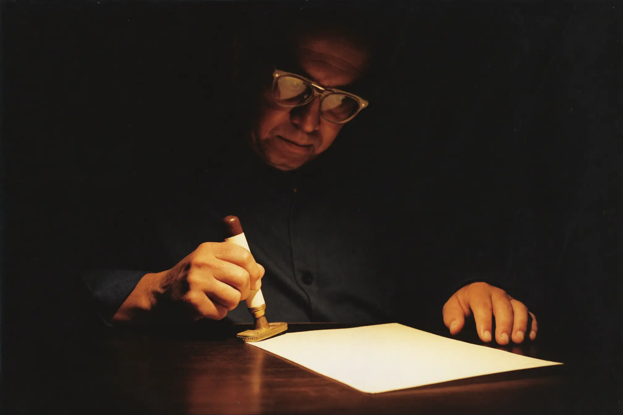 A desk clerk stamping a blank form at a dark wooden counter.
