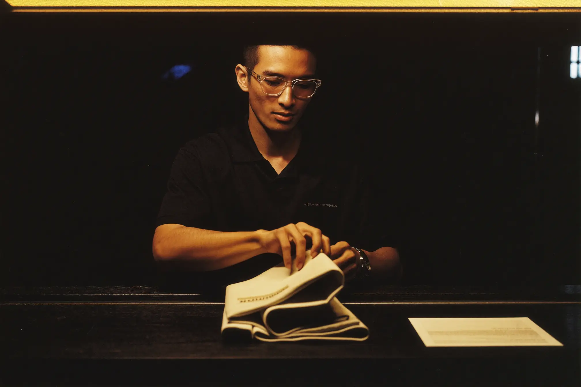 A retail salesman arranging folded fabric on a dark wooden display.