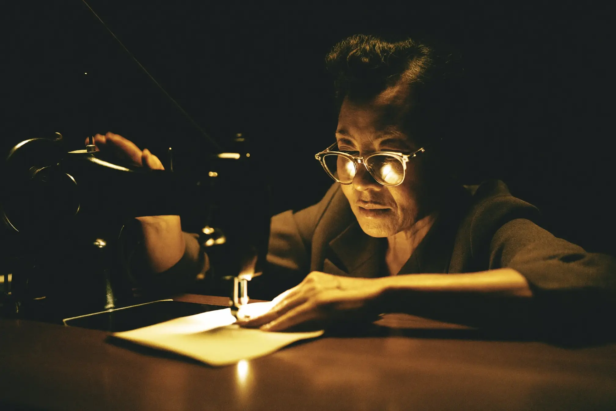 A tailor guiding fabric under the needle of a dark sewing machine.