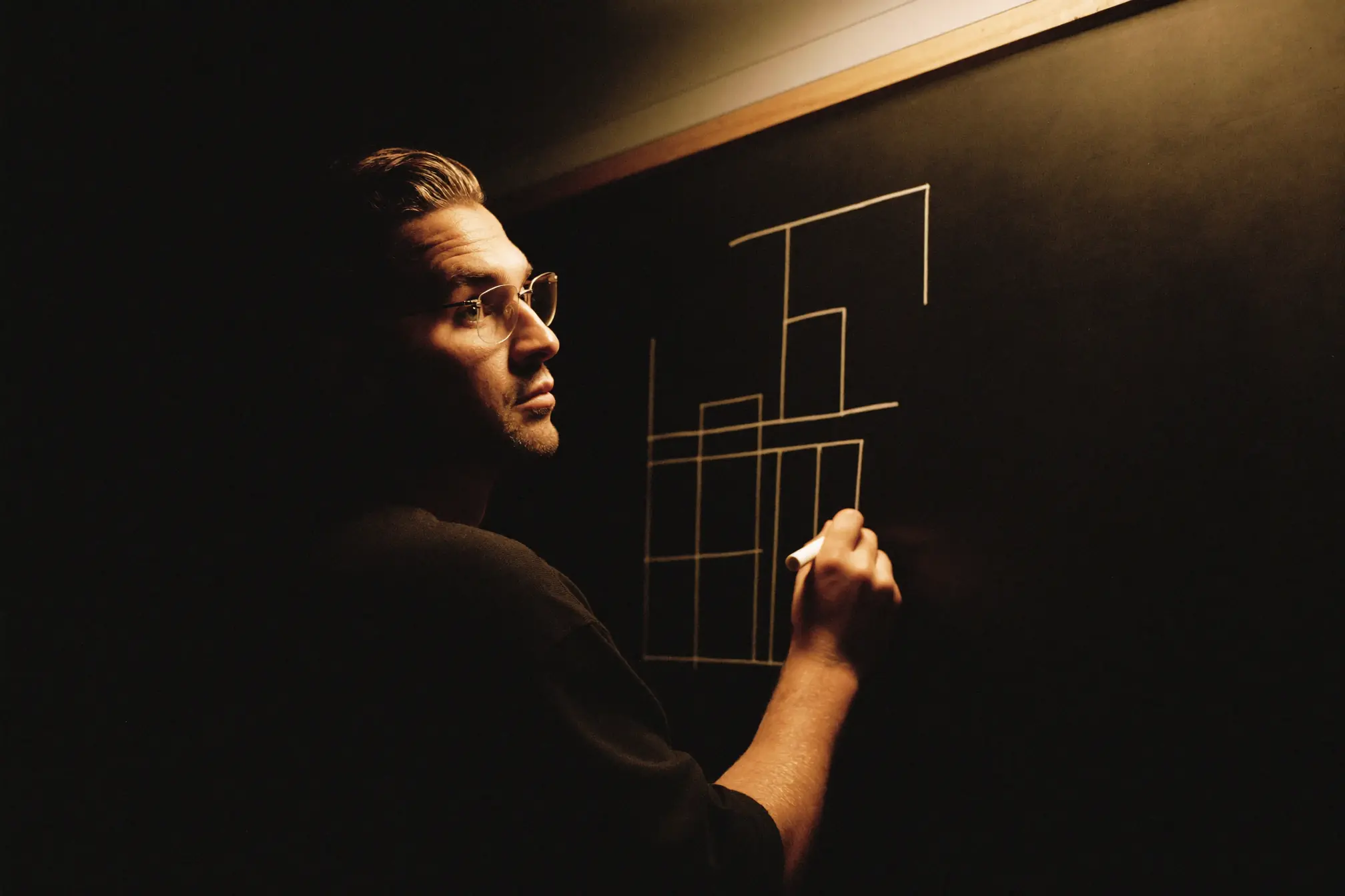 A technical architect sketching boxes and lines on a dark whiteboard.