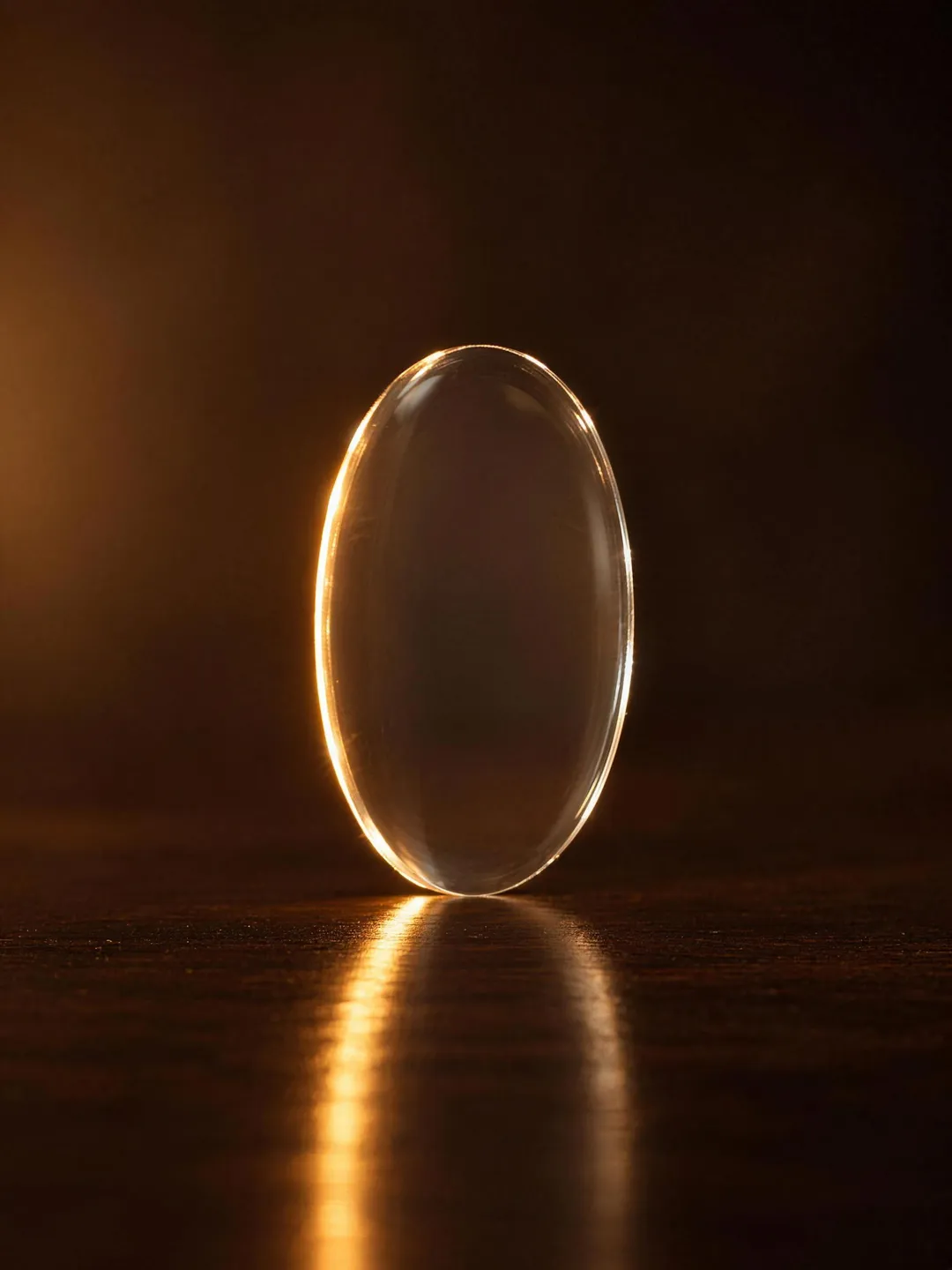 A thin finished lens standing on its edge on a dark surface, its slim polished rim catching the light, the CLIFF mark etched faintly on the glass.